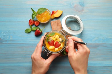 Photo of Woman eating delicious mango jelly with fresh fruits  at light blue wooden table, top view