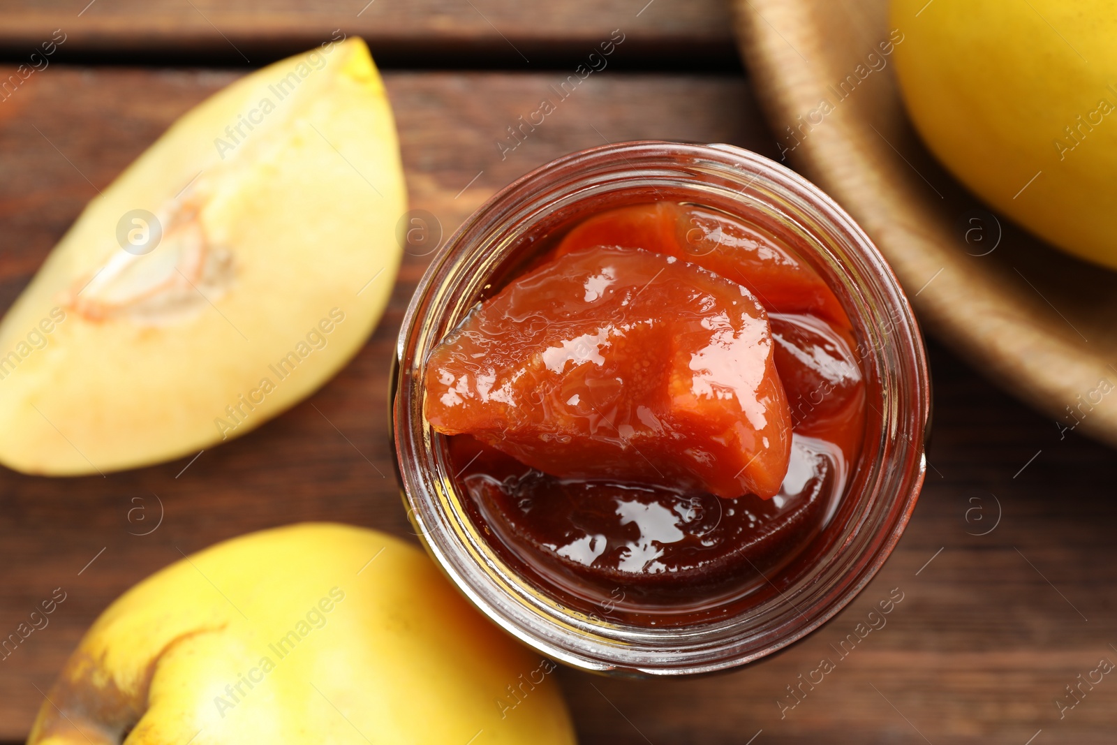 Photo of Tasty homemade quince jam in jar and fruits on wooden table, top view