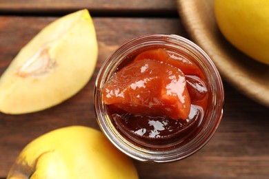 Tasty homemade quince jam in jar and fruits on wooden table, top view