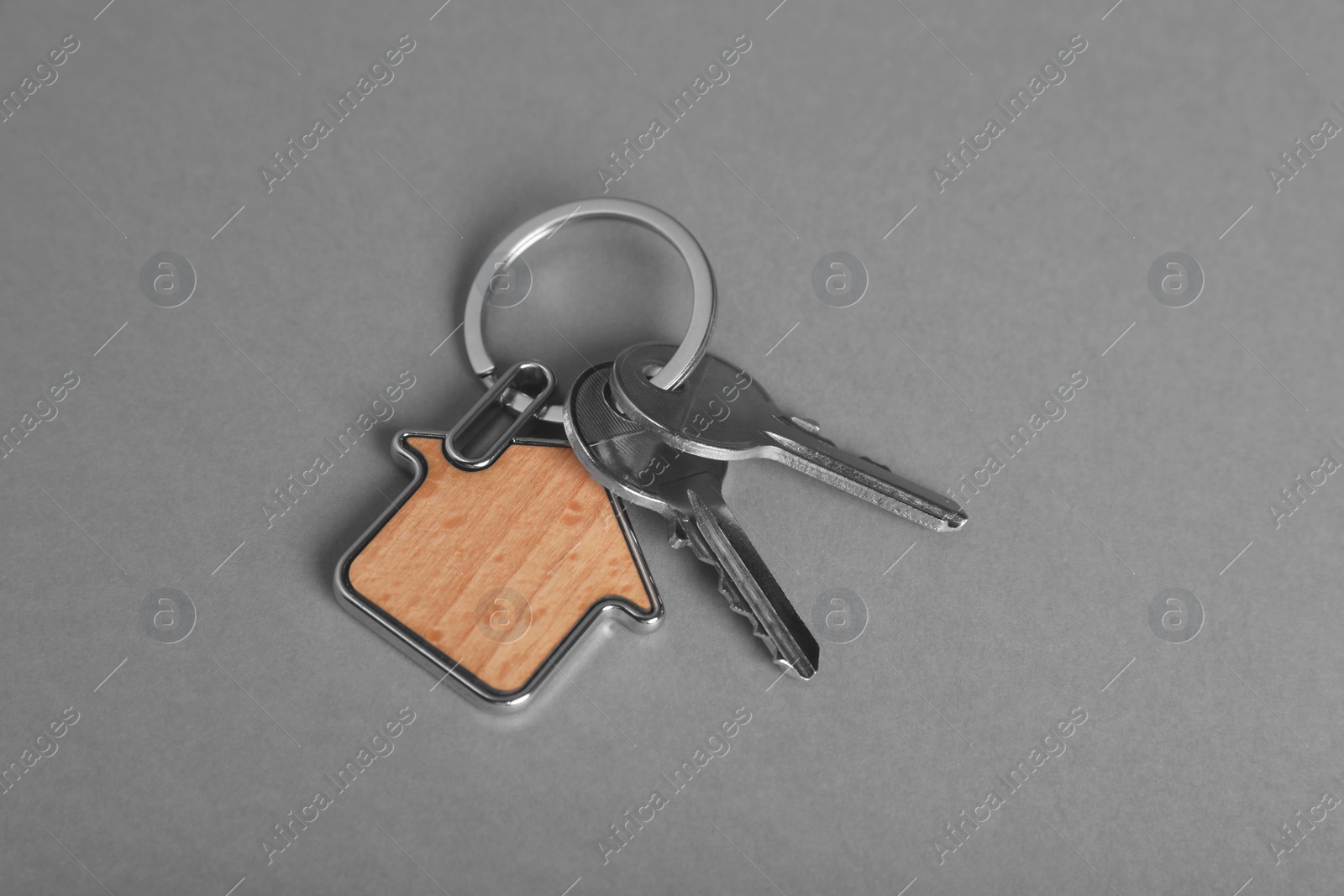 Photo of Keys with trinket in shape of house on grey background, above view. Real estate agent services