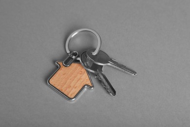 Keys with trinket in shape of house on grey background, above view. Real estate agent services