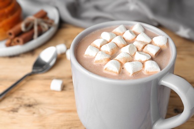 Photo of Delicious hot cocoa drink with marshmallows in cup on wooden table, closeup