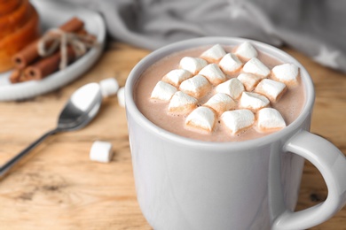 Delicious hot cocoa drink with marshmallows in cup on wooden table, closeup