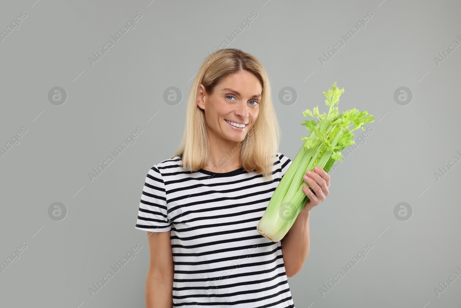 Photo of Woman holding fresh green celery bunch on light grey background