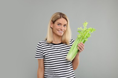 Photo of Woman holding fresh green celery bunch on light grey background