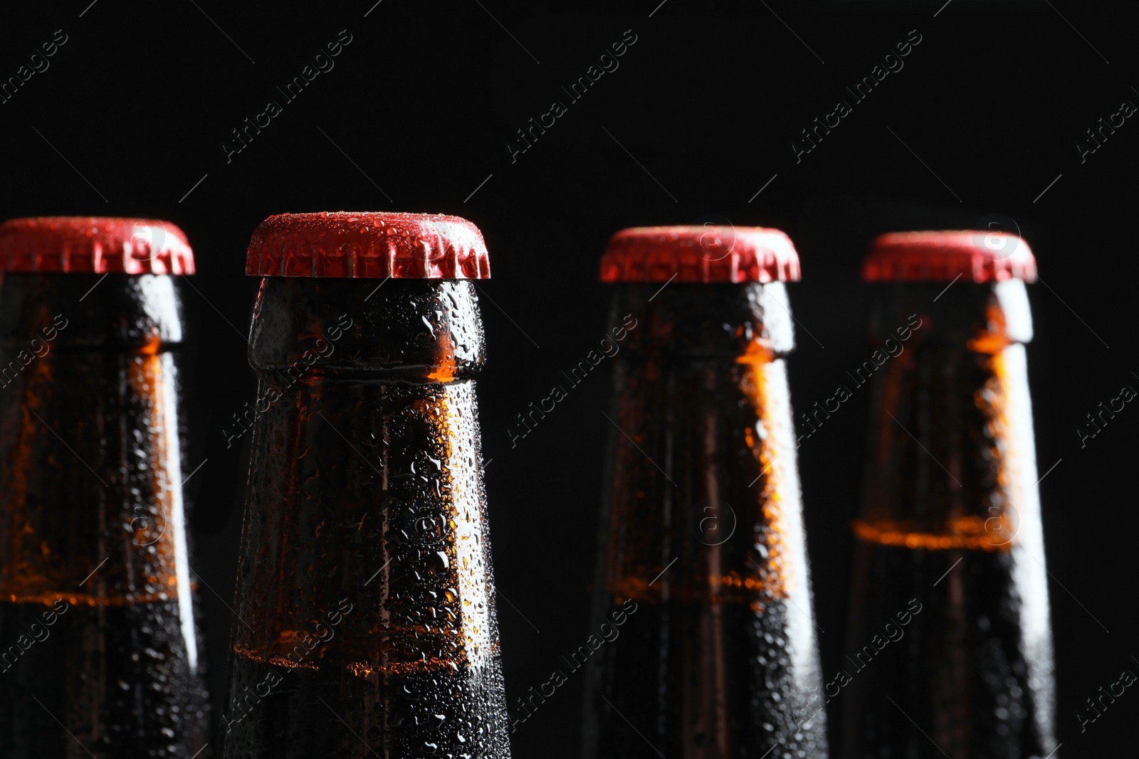 Photo of Bottles of tasty cold beer on black background, closeup