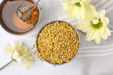 Fresh bee pollen granules, flowers, honey and dipper on white table, flat lay
