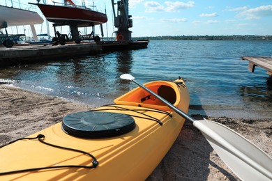 Photo of Yellow kayak with paddle on beach near river, closeup. Summer camp activity