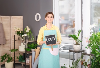 Photo of Female florist holding OPEN sign at workplace