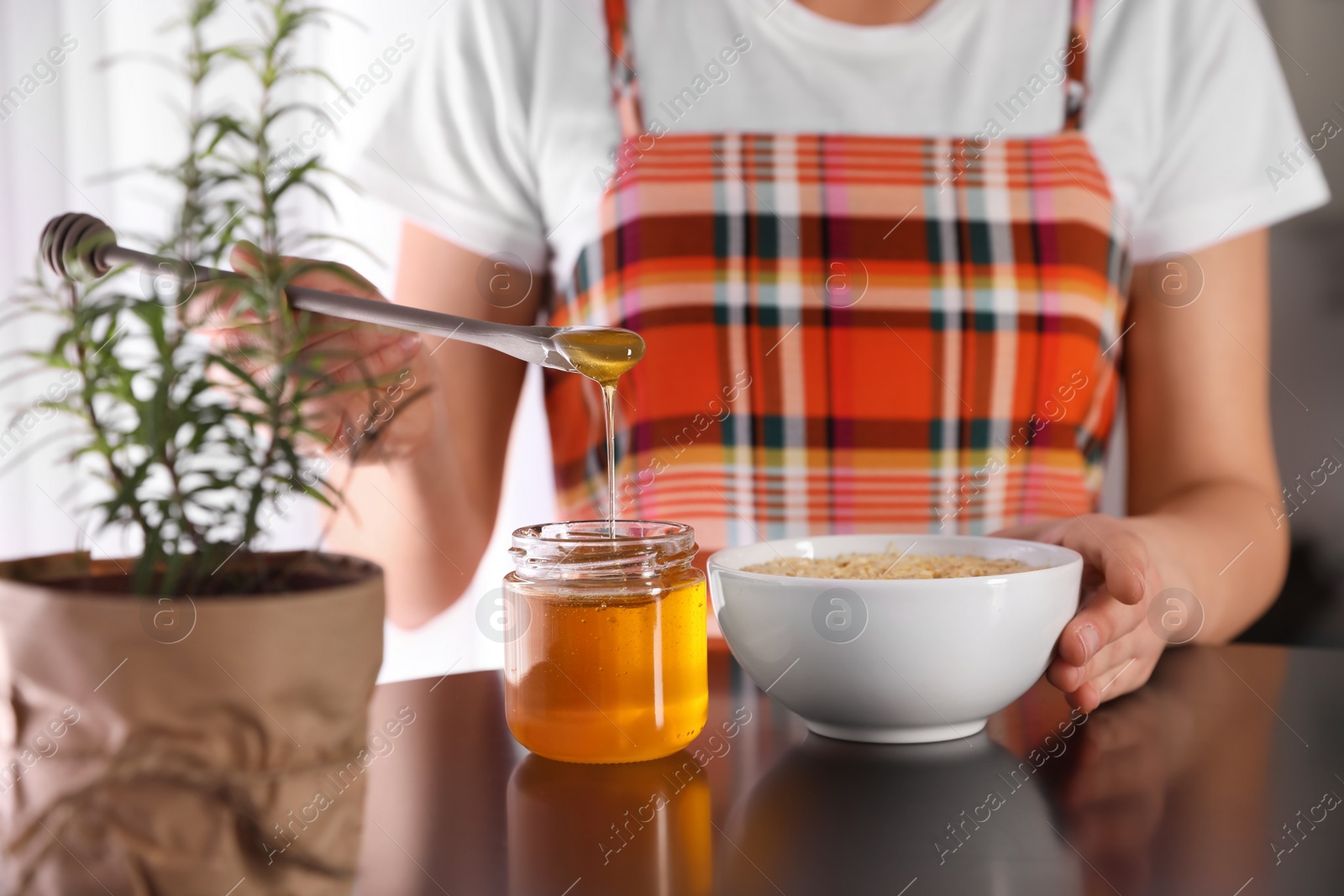 Photo of Woman adding honey to oatmeal at black table, closeup