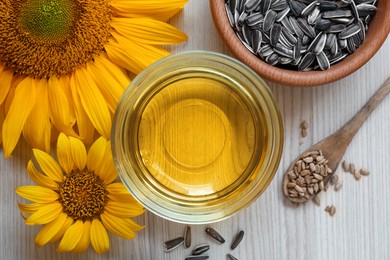 Photo of Sunflower oil in glass bowl and seeds on wooden table, flat lay