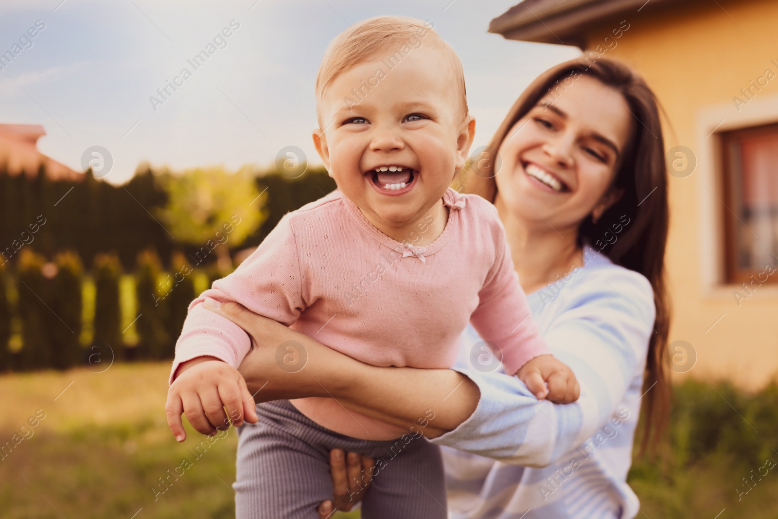 Image of Happy mother playing with her cute baby at backyard on sunny day