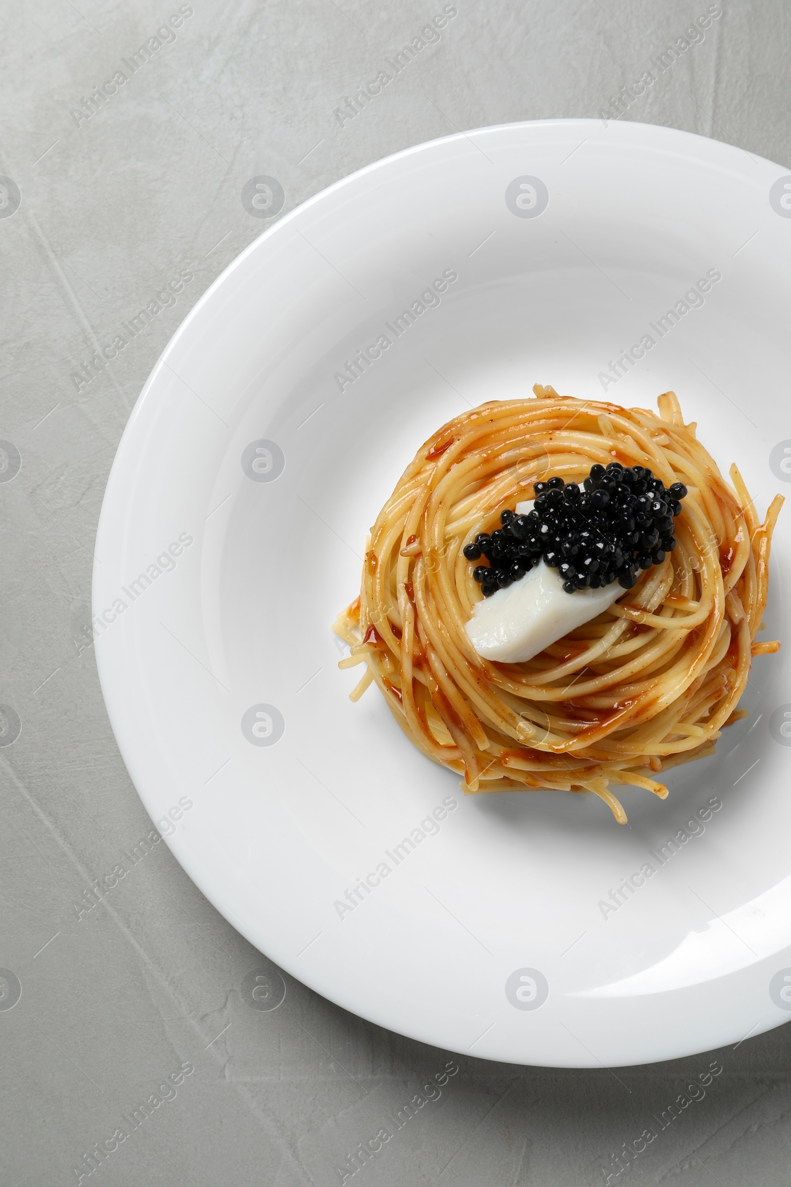 Photo of Tasty spaghetti with tomato sauce and black caviar on light grey table, top view. Exquisite presentation of pasta dish