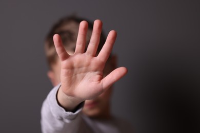 Child abuse. Boy doing stop gesture on gray background, selective focus. Space for text