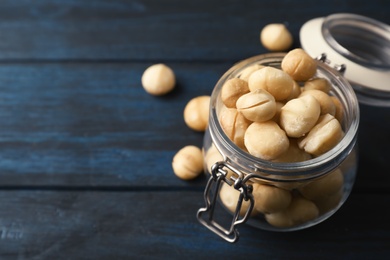 Jar with shelled organic Macadamia nuts and space for text on blue wooden background