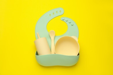 Photo of Baby feeding accessories and bib on yellow background, top view