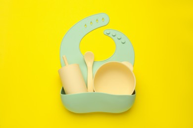 Baby feeding accessories and bib on yellow background, top view