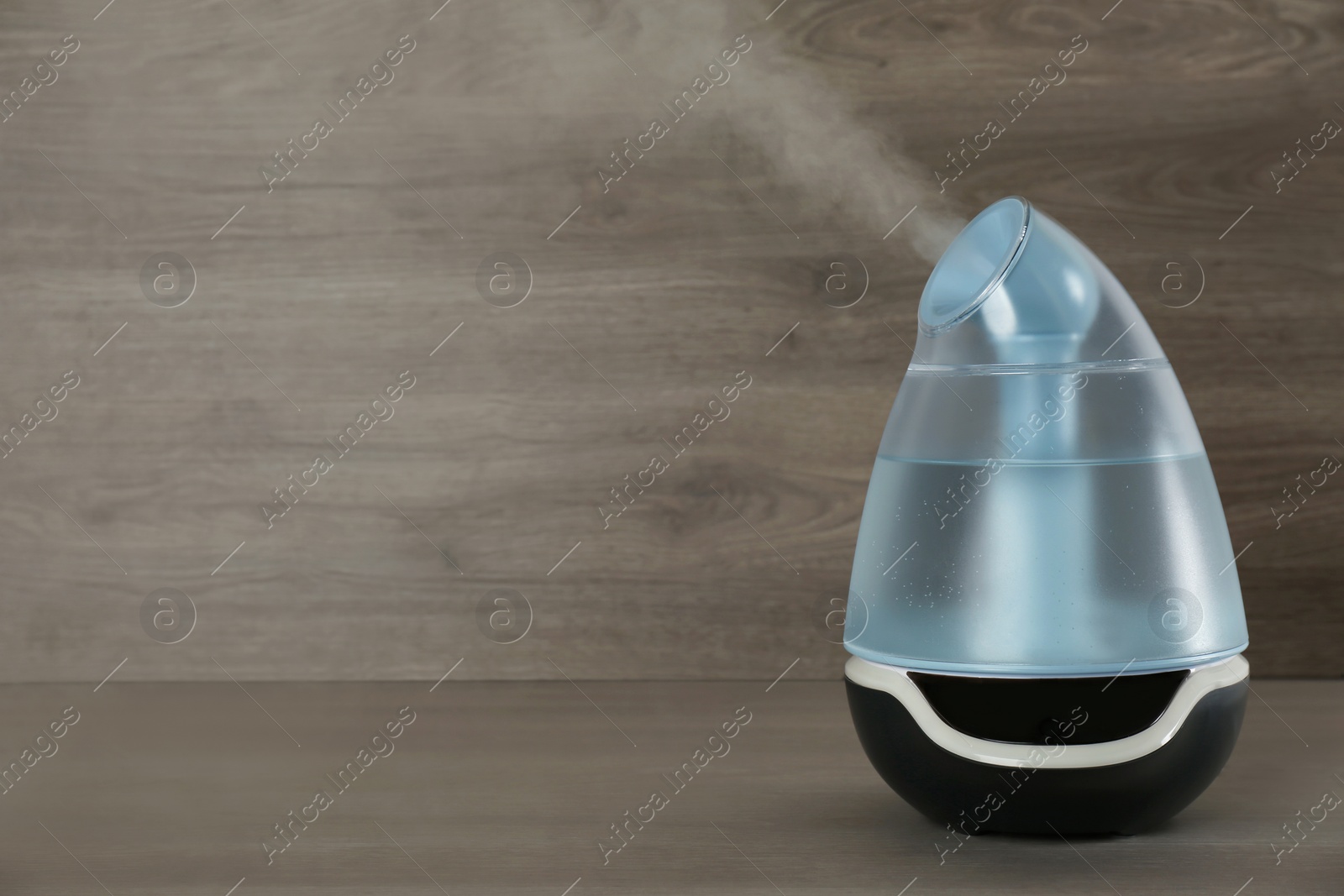 Photo of Modern air humidifier on wooden table. Space for text