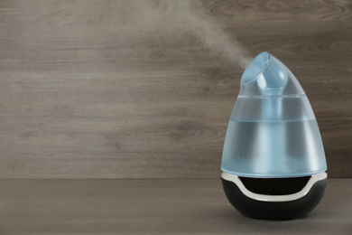 Photo of Modern air humidifier on wooden table. Space for text