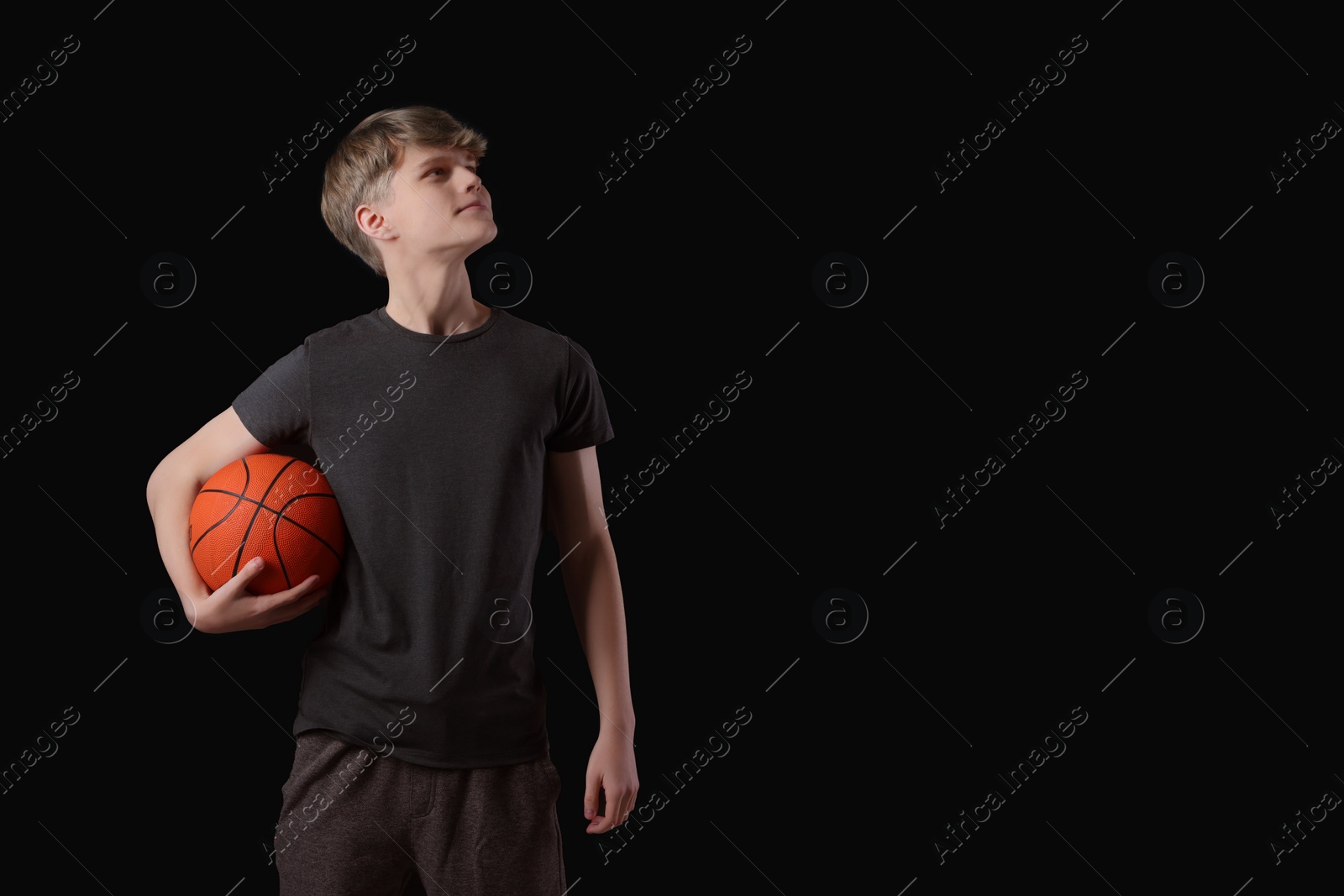 Photo of Teenage boy with basketball ball on black background. Space for text