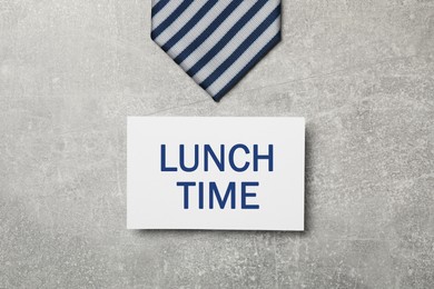 Image of Business lunch. Card with phrase Lunch Time and striped tie on light gray textured background, flat lay