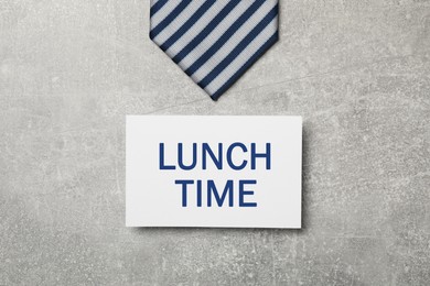 Business lunch. Card with phrase Lunch Time and striped tie on light gray textured background, flat lay