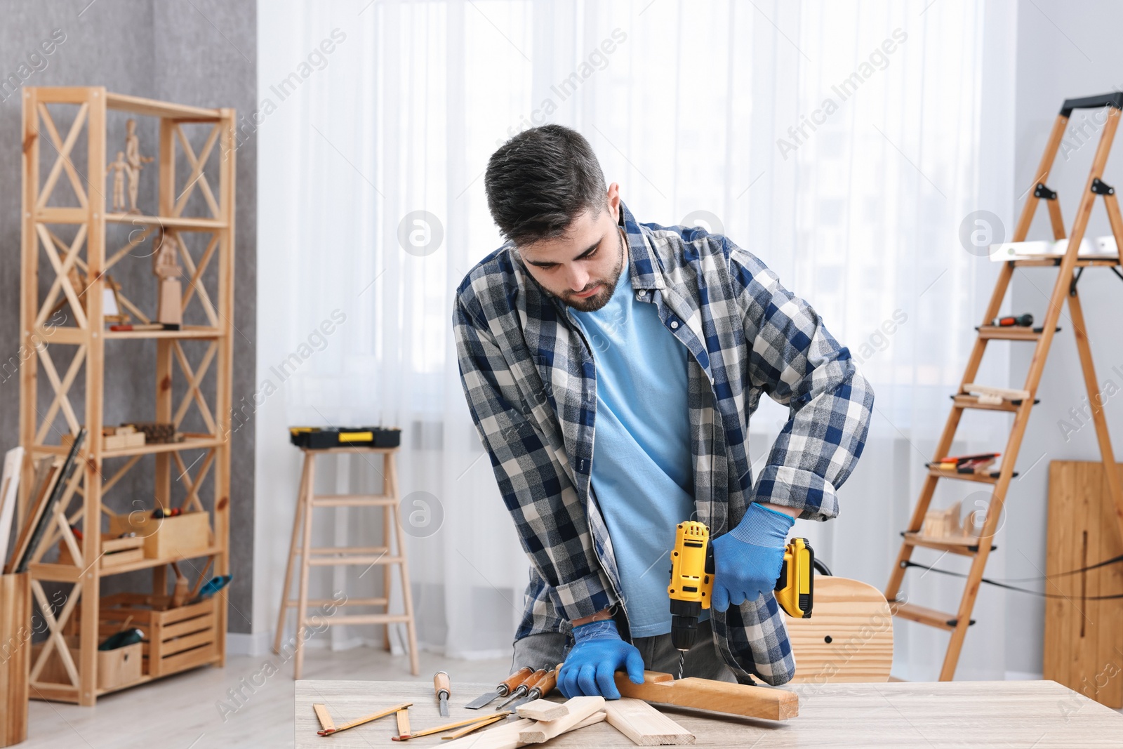 Photo of Young handyman working with electric drill at table in workshop