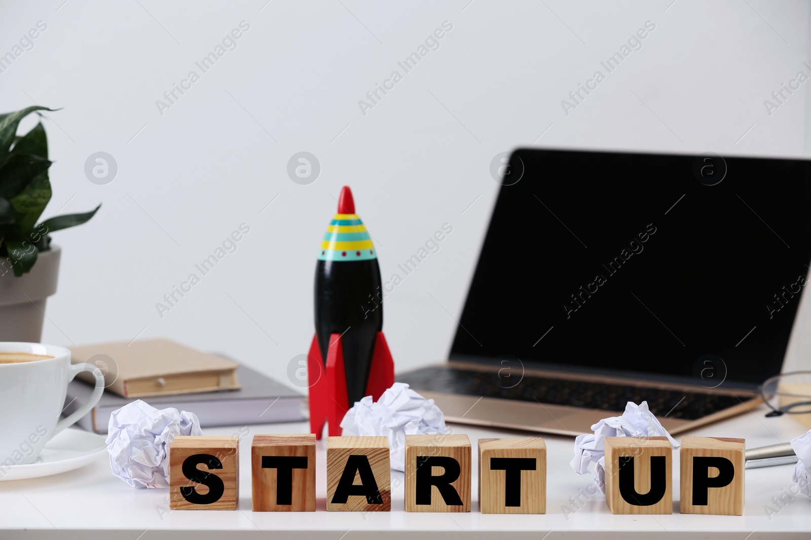 Photo of Wooden cubes with words Start Up and toy rocket on messy table indoors