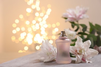 Photo of Bottle of perfume and beautiful lily flowers on table against beige background with blurred lights, closeup. Space for text