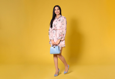 Young woman wearing floral print dress with stylish handbag on yellow background