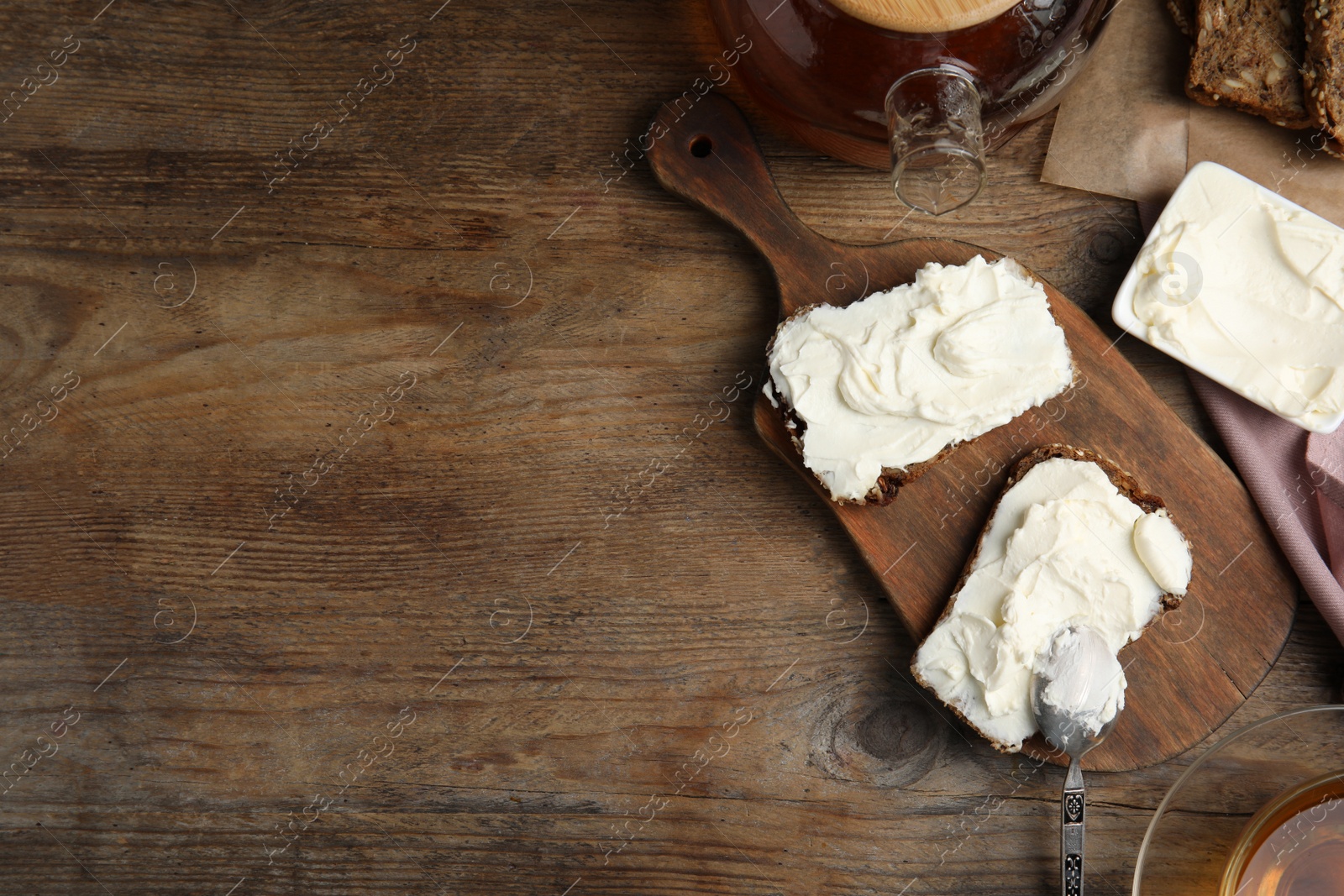Photo of Bread with cream cheese on wooden table, flat lay. Space for text