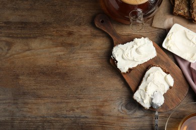 Photo of Bread with cream cheese on wooden table, flat lay. Space for text