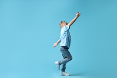 Photo of Happy little boy dancing on light blue background. Space for text