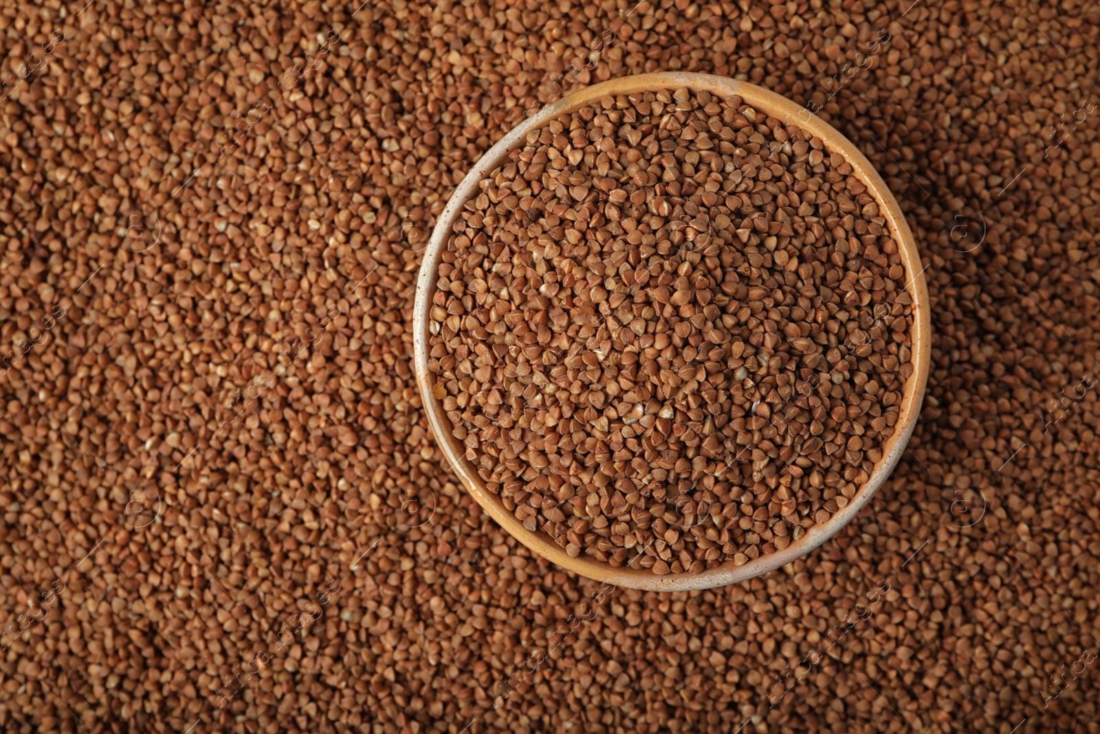 Photo of Uncooked buckwheat in bowl on grains, top view. Space for text