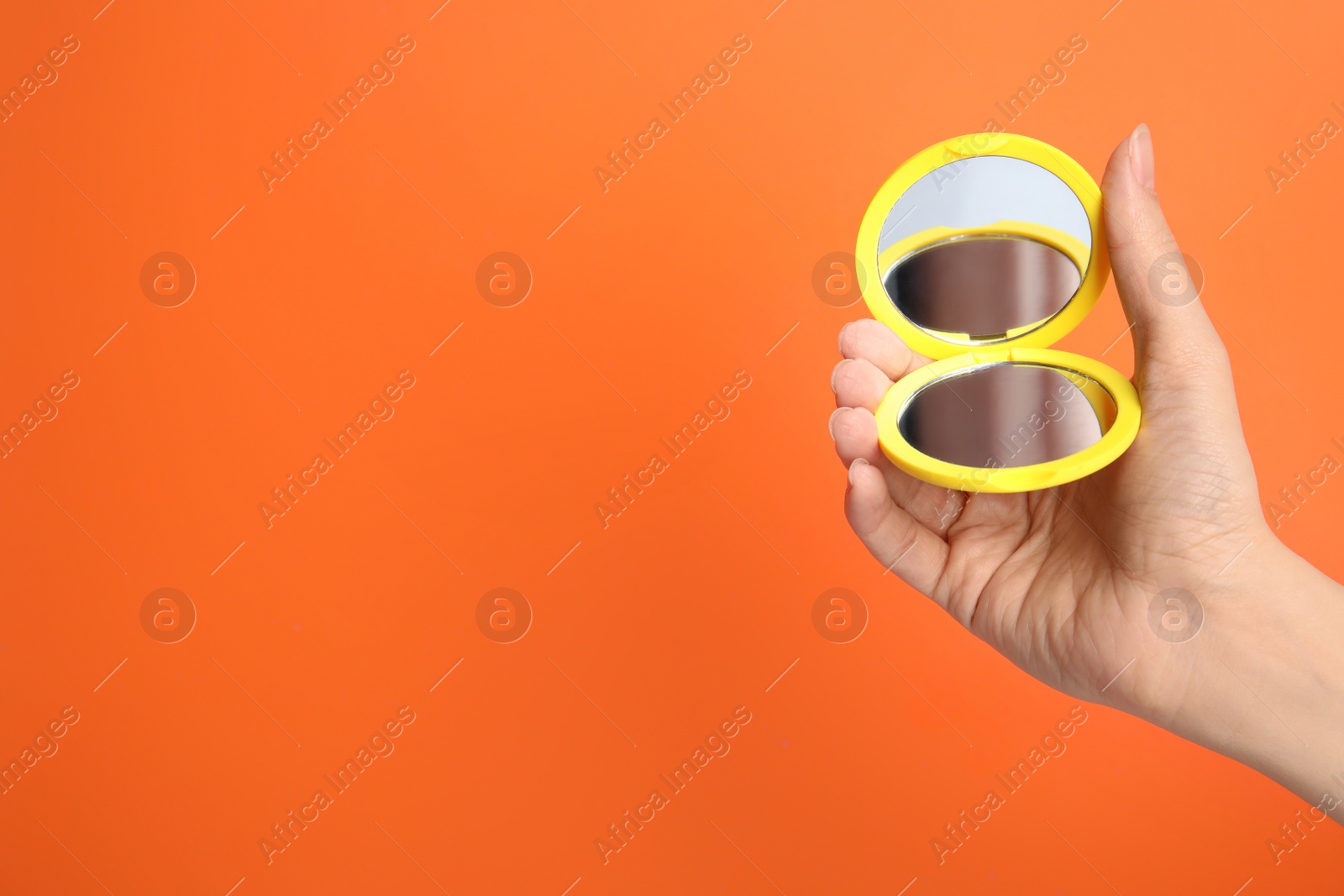 Photo of Woman holding stylish cosmetic pocket mirror on orange background, closeup. Space for text