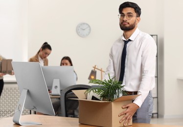Photo of Unemployment problem. Frustrated man with box of personal belongings at table in office