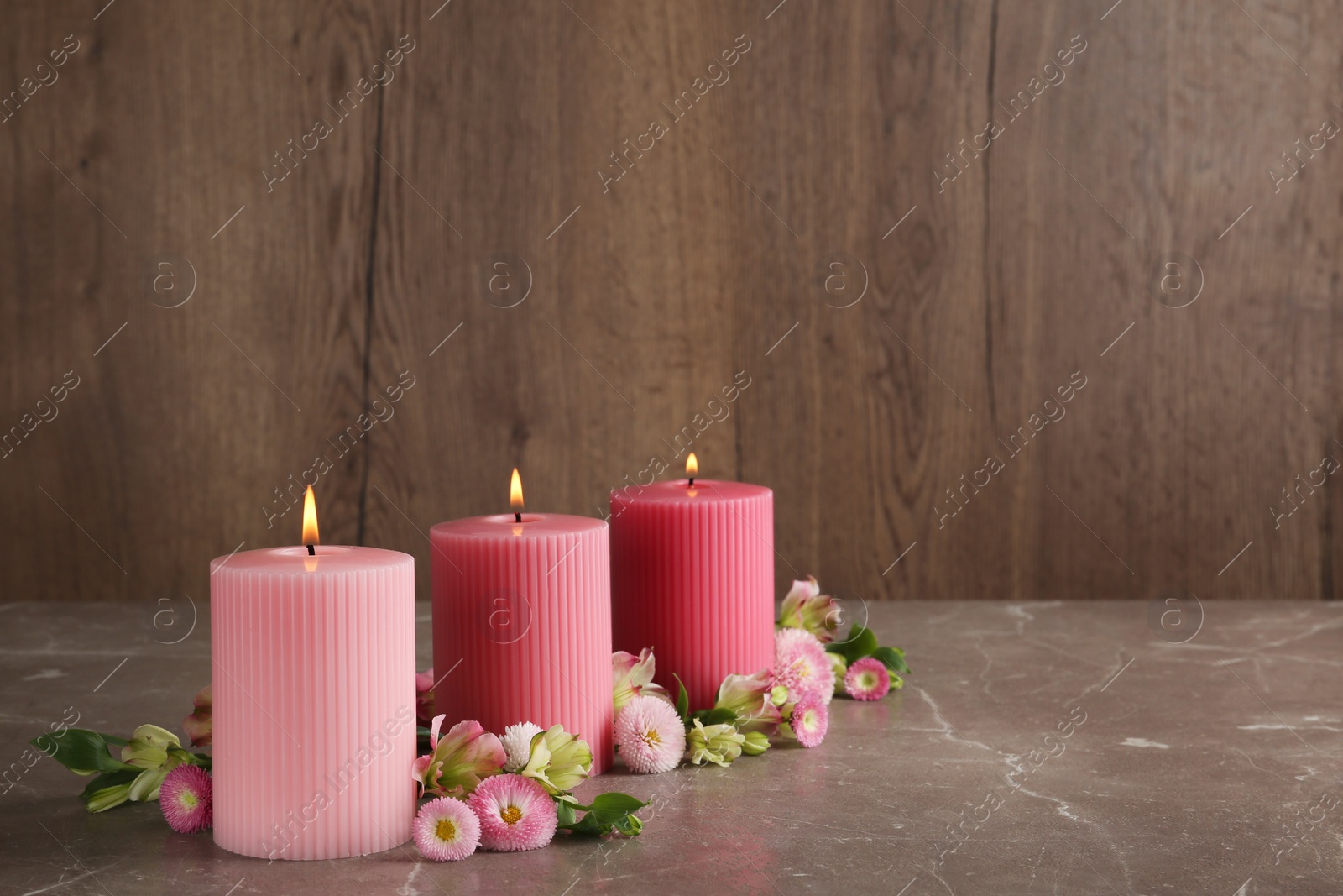 Photo of Stylish tender composition with burning candles and flowers on table against wooden background, space for text. Cozy interior element