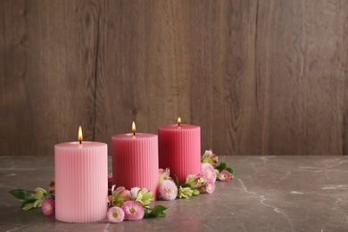 Photo of Stylish tender composition with burning candles and flowers on table against wooden background, space for text. Cozy interior element