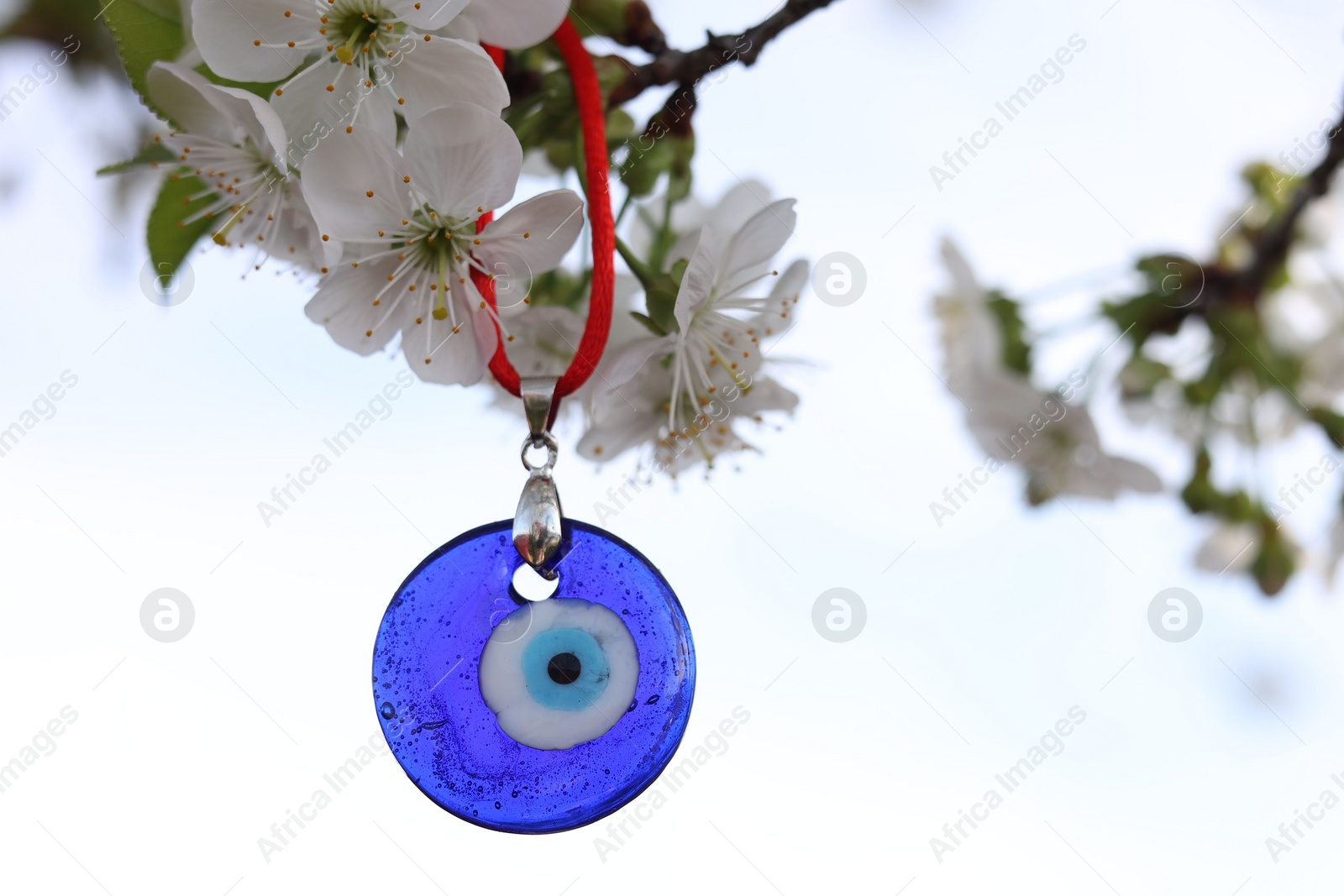 Photo of Evil eye amulet hanging on blossoming spring tree outdoors. Space for text