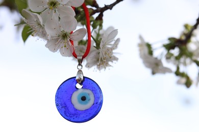 Evil eye amulet hanging on blossoming spring tree outdoors. Space for text