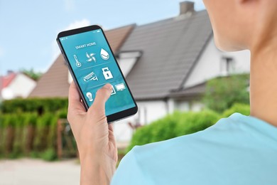 Image of Woman using smart home control system via mobile phone near house outdoors, closeup