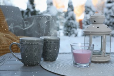 Photo of Candle, lantern and cups with hot drink on coffee table outdoors. Cosy winter