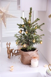 Small Christmas tree decorated with baubles and festive lights in kitchen