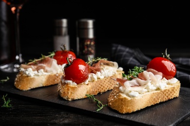 Slate plate of delicious bruschettas with prosciutto on black wooden table