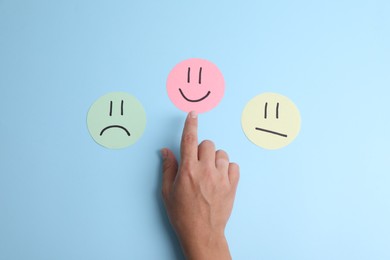 Photo of Choice concept. Woman choosing paper with happy emoticon among others on light blue background, top view