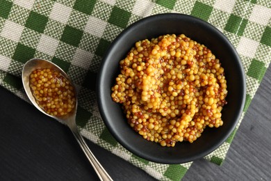 Bowl and spoon with whole grain mustard on black wooden table, flat lay