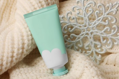 Winter skin care. Hand cream and decorative snowflake on white knitted sweater, closeup