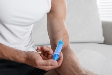 Photo of Athletic man injecting himself on sofa indoors, closeup. Doping concept