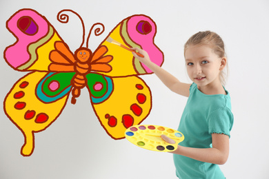 Cute child drawing butterfly on white wall indoors