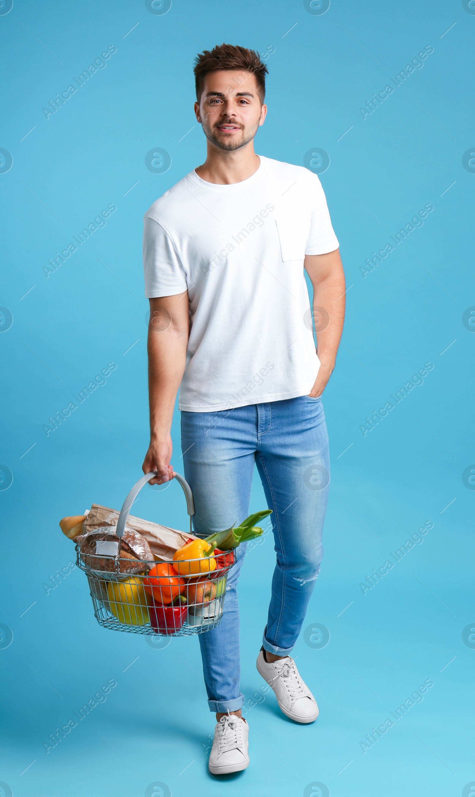 Photo of Young man with shopping basket full of products on blue background